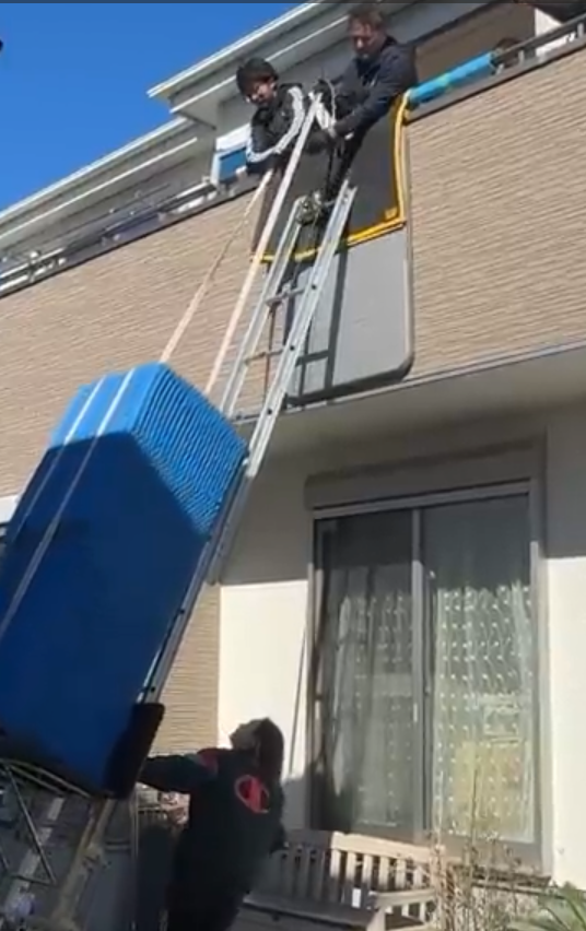 Workers receiving a large refrigerator from a powered ladder at a second-floor window