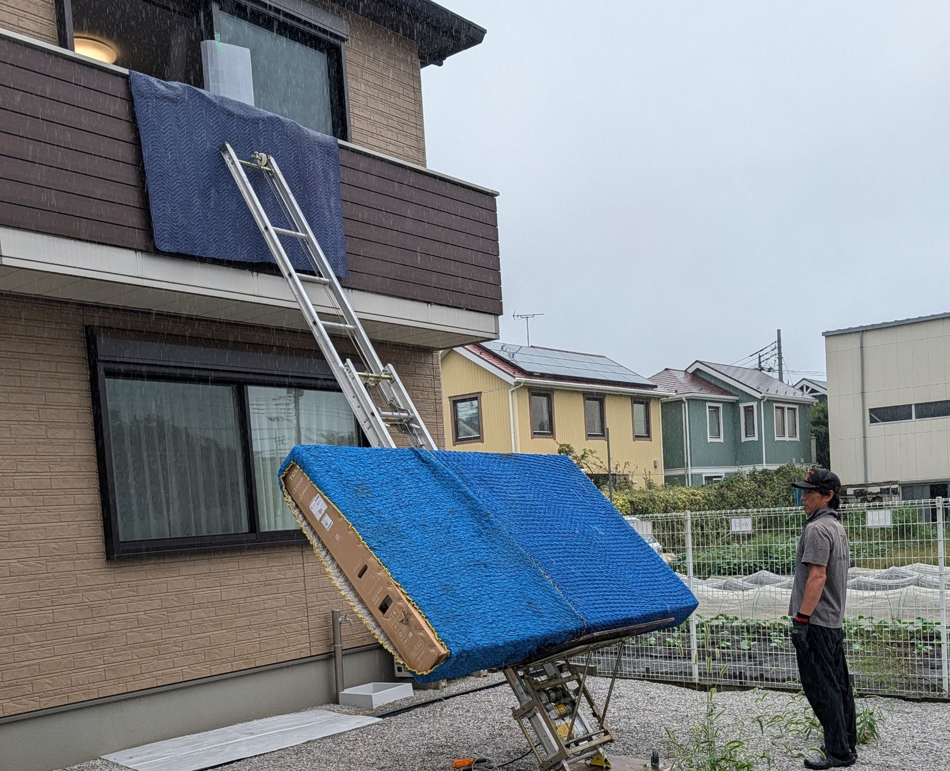 A large appliance being brought to the second floor on a powered ladder in the rain