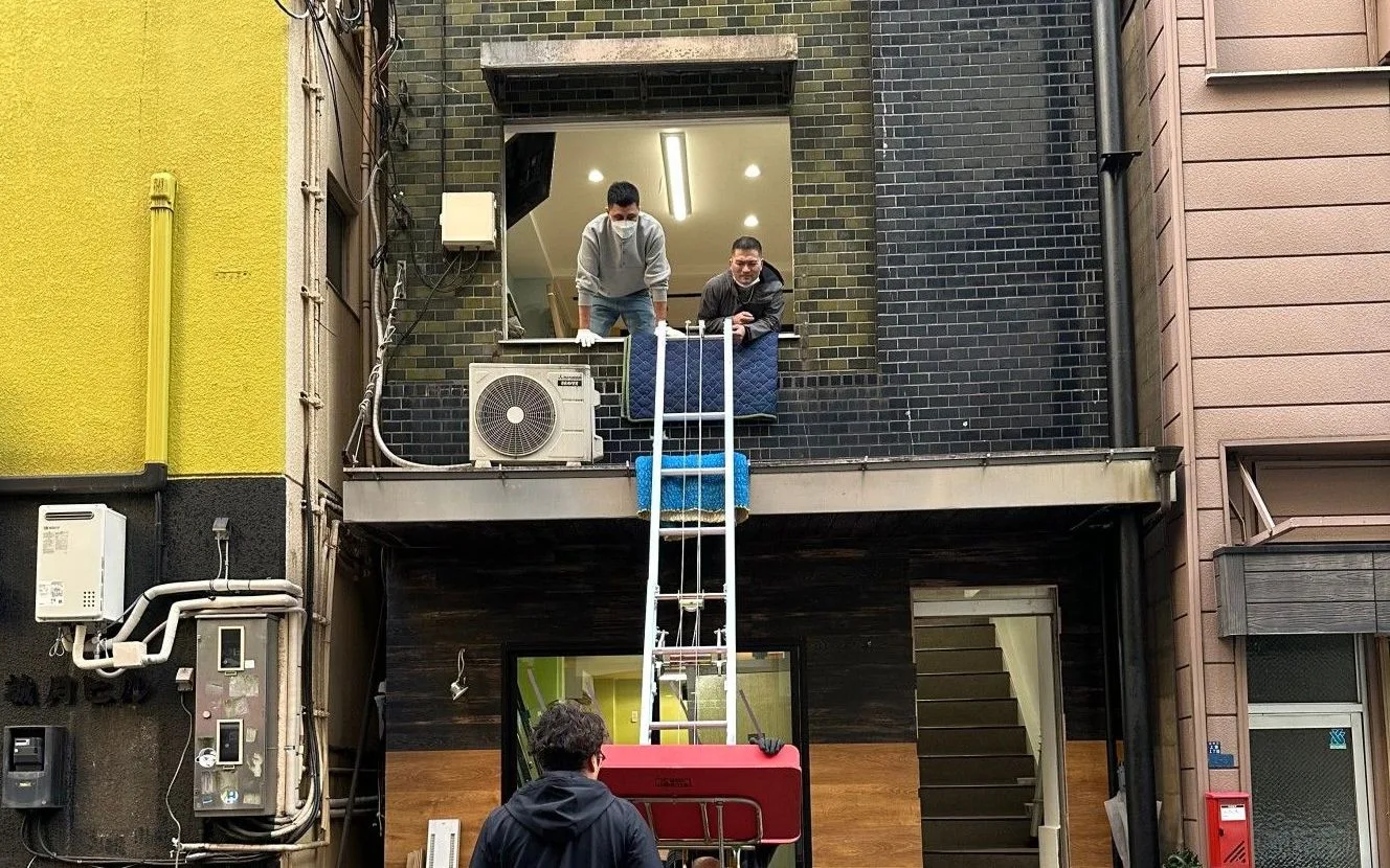 Workers using a powered ladder to bring a bed mattress through a second-floor window